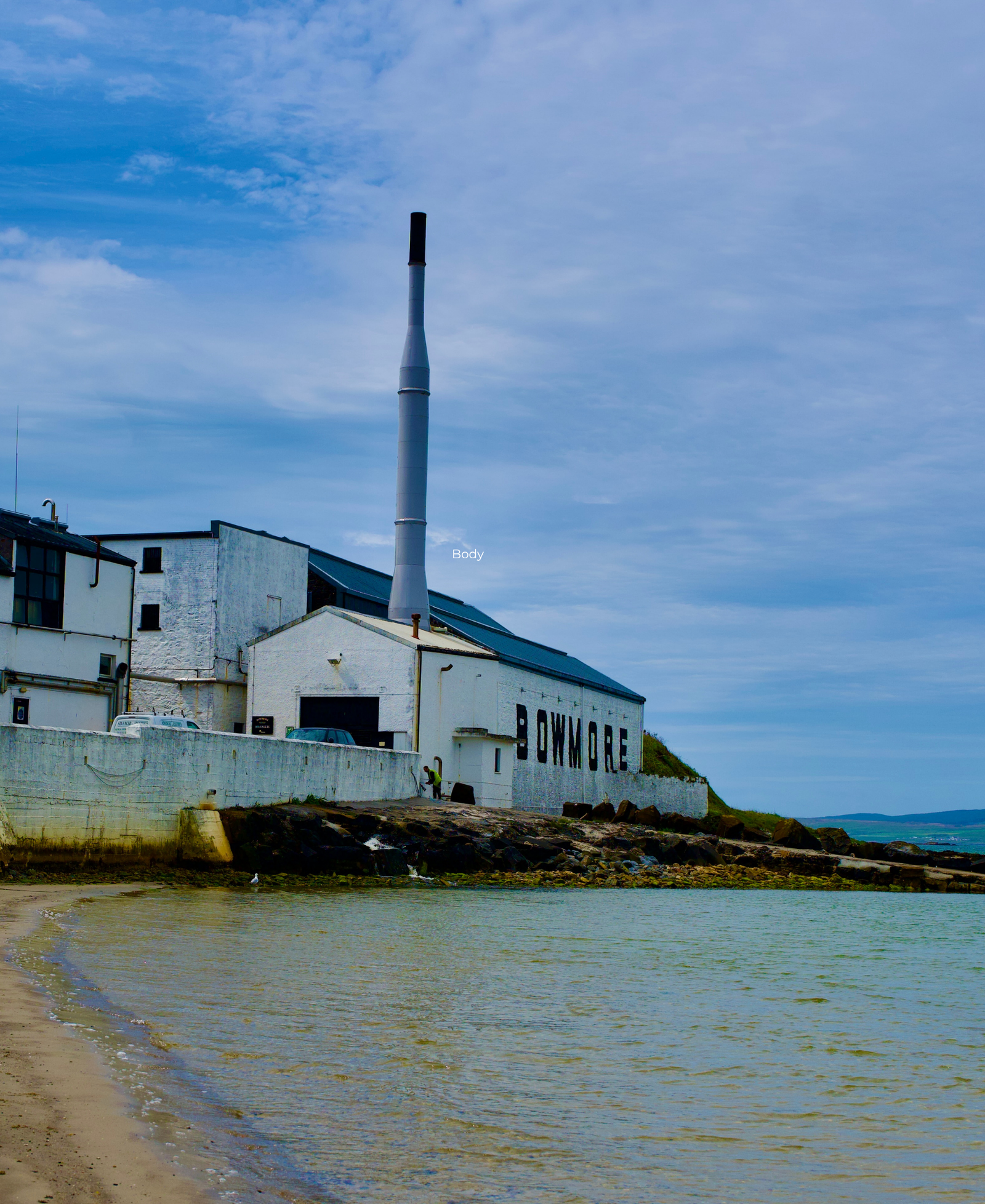 Bowmore Distillery, Islay Bowmore whisky distillery on the shoreline of Islay, with its tall chimney and 'Bowmore' sign visible above the beach