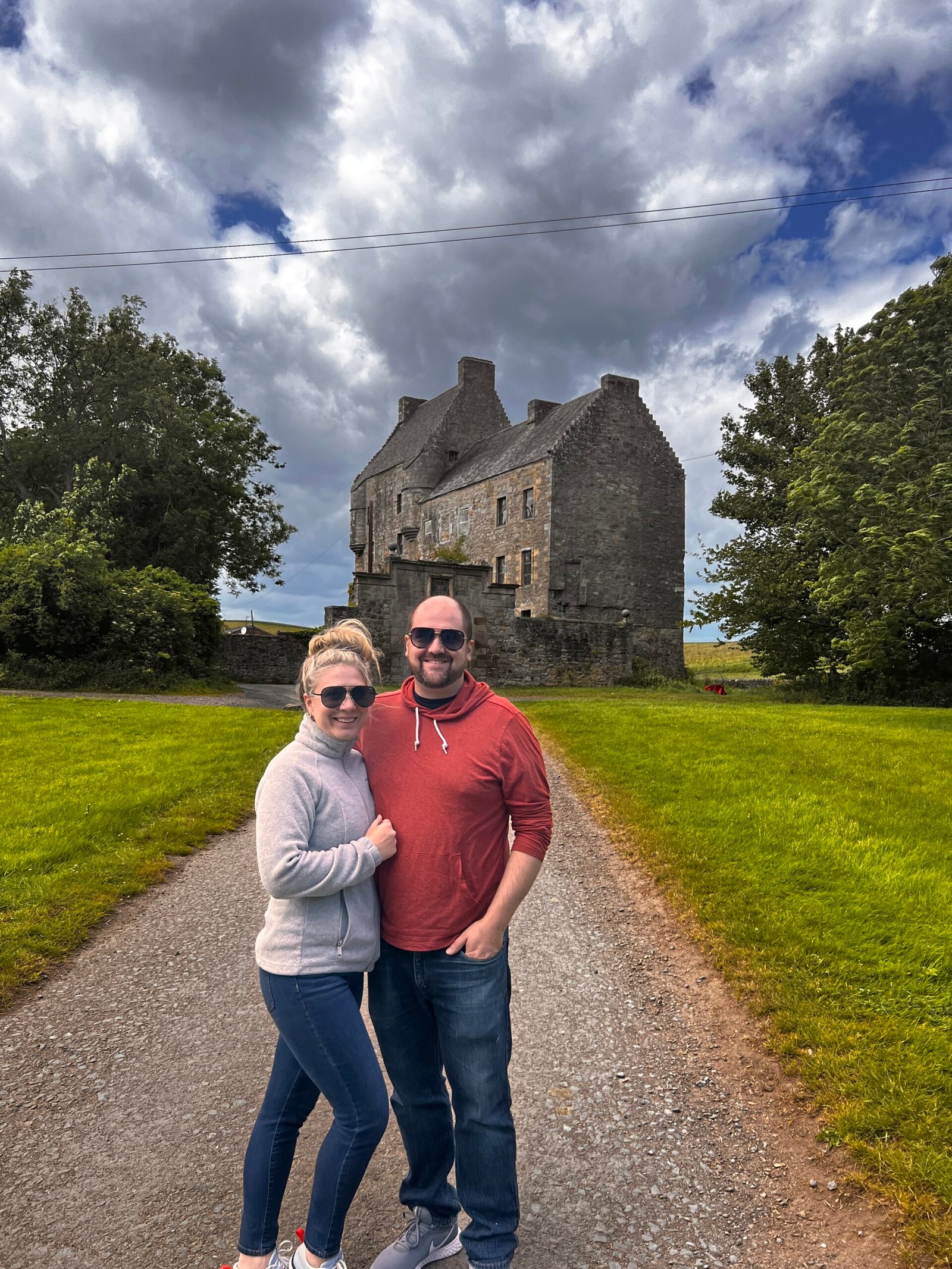 Couple standing on a path in front of Midhope Castle under a dramatic cloudy sky
