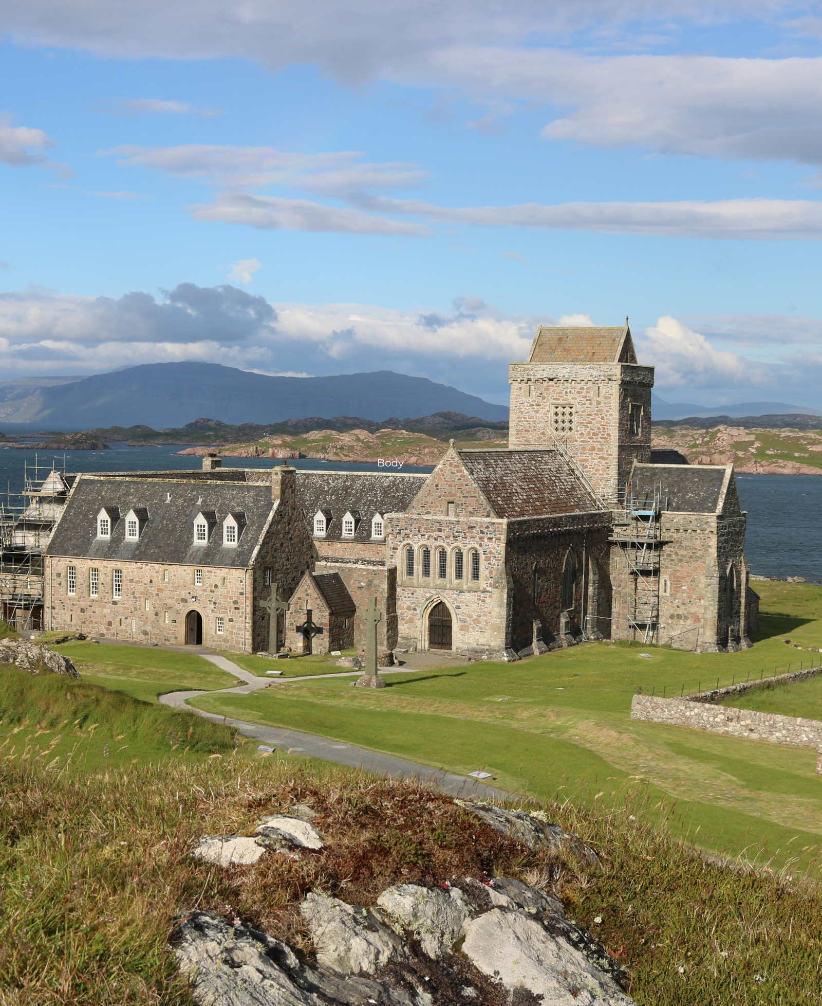 Iona Abbey and its stone tower on the Isle of Iona, with Celtic crosses in the foreground and hills across the water