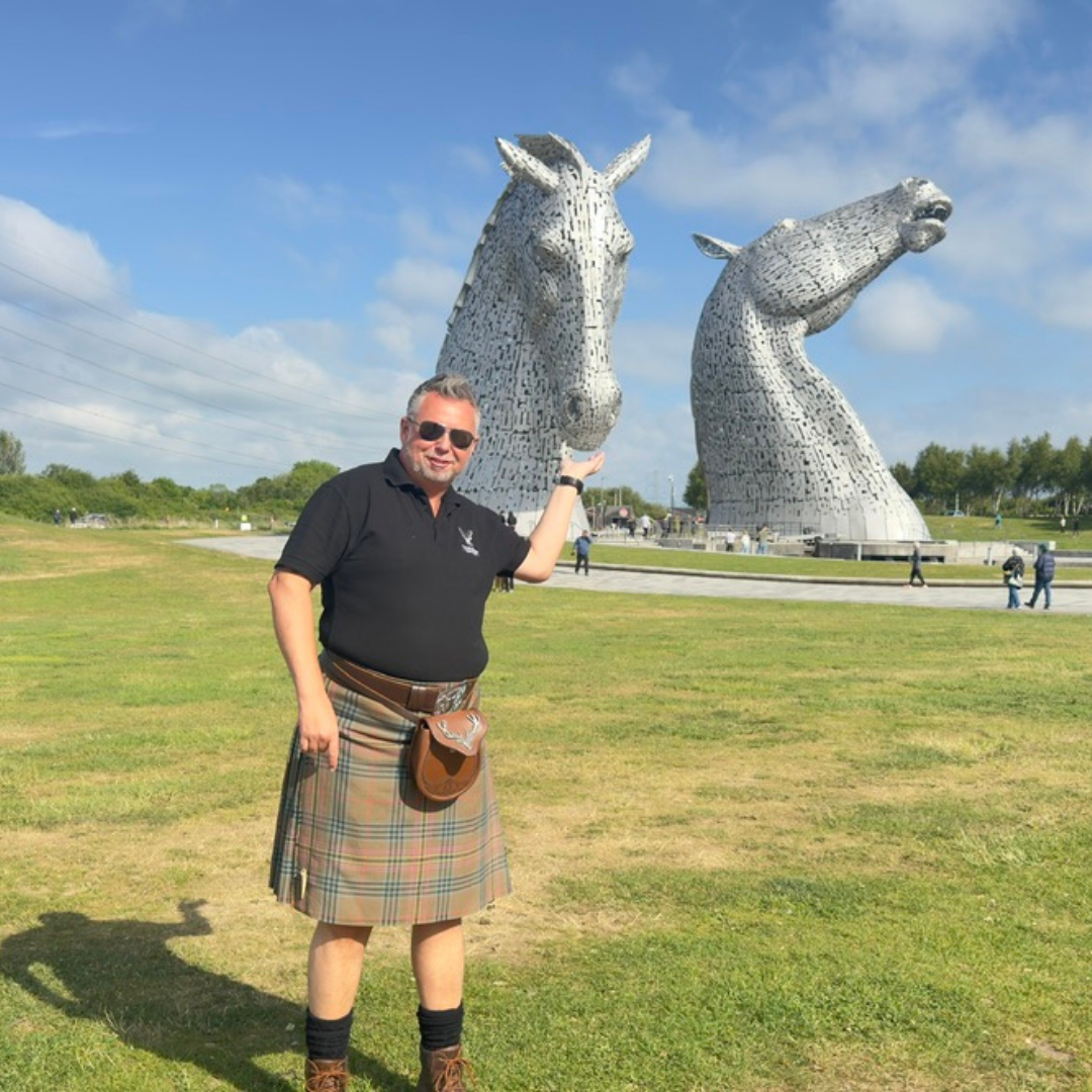 James Feeding the Kelpies James from Tour Guide Scotland posing playfully with the Kelpies sculptures in Falkirk, as if feeding one of the horse heads