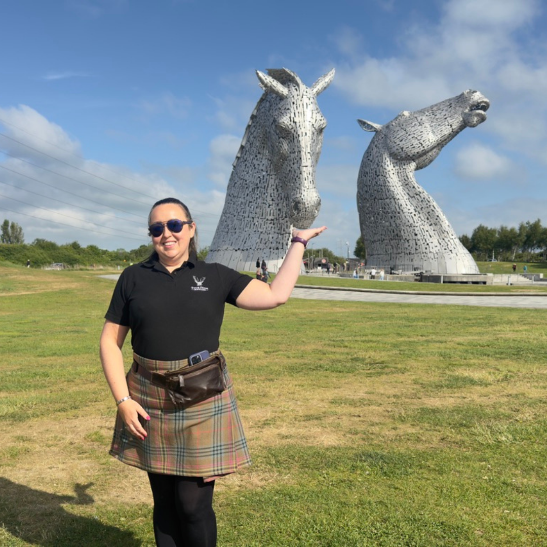 Lesley Feeding the Kelpies Lesley from Tour Guide Scotland posing playfully with the Kelpies sculptures in Falkirk, as if feeding one of the horse heads