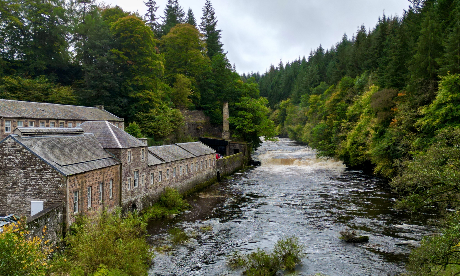 New Lanark The historic mill buildings of New Lanark alongside the River Clyde, with a weir and wooded gorge in the background