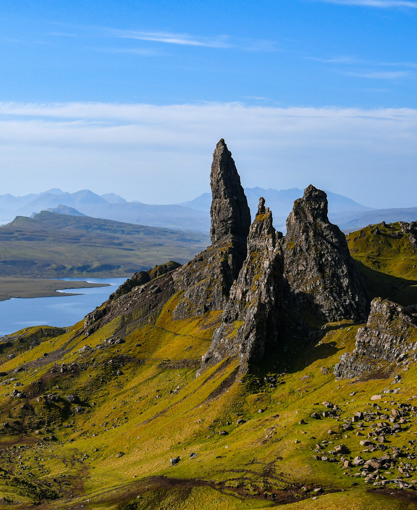The Old Man of Storr rock pinnacle on the Isle of Skye, with a loch and misty mountains in the distance