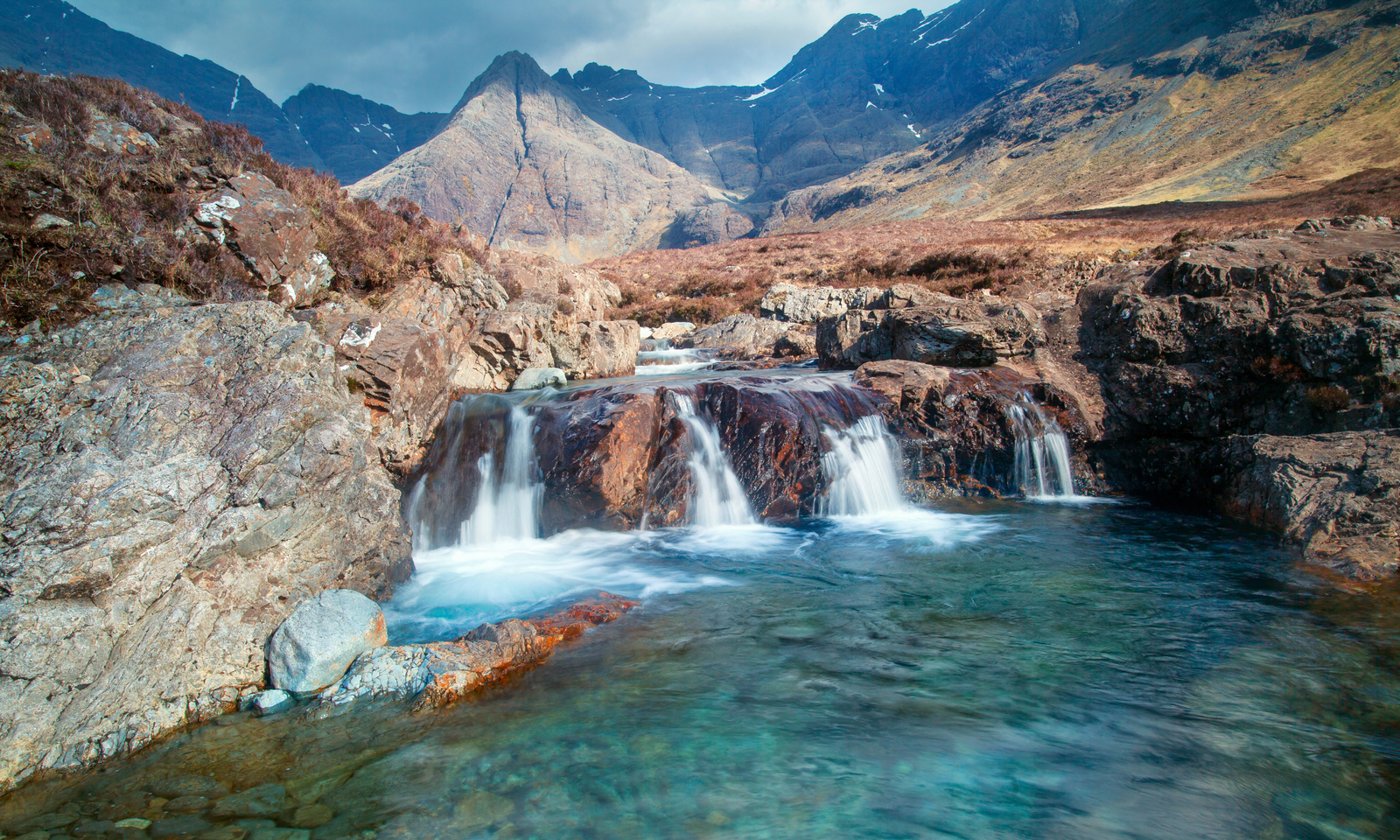 Crystal-clear turquoise pools and waterfalls at the Fairy Pools on Skye, with the Black Cuillin mountains behind