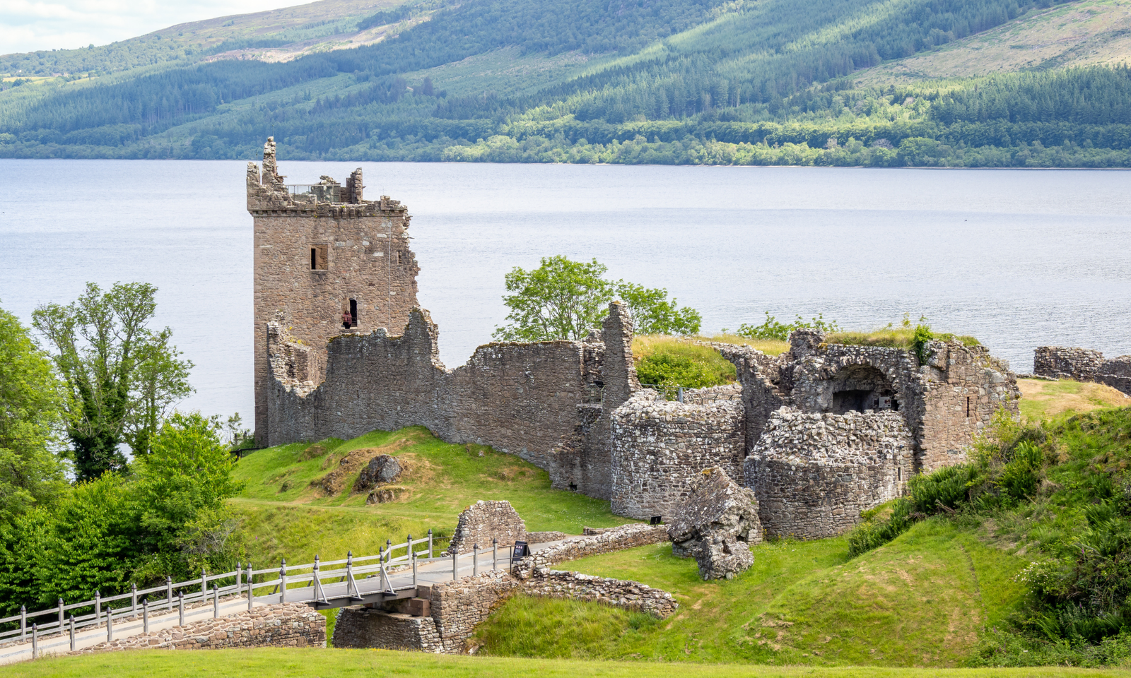 Urquhart Castle Ruins of Urquhart Castle on the shore of Loch Ness, with a stone bridge leading to the site and forested hills beyond