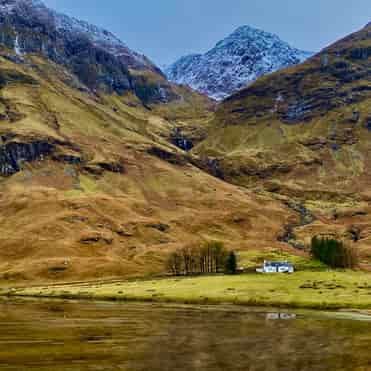 Cottage Beneath the Mountains, Glencoe Remote white cottage against snow-capped peaks in Glencoe, Scotland