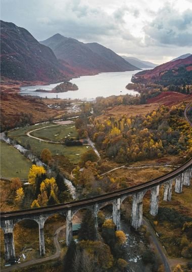 The Glenfinnan Viaduct curving through the Scottish Highlands, with Loch Shiel and autumn-coloured hills in the background
