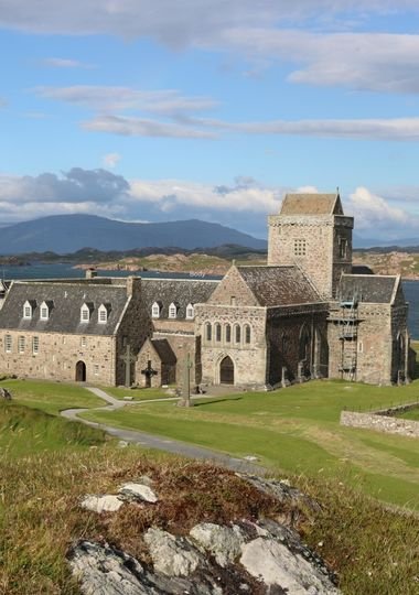 Iona Abbey and its stone tower on the Isle of Iona, with Celtic crosses in the foreground and hills across the water