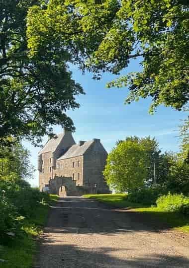 Midhope Castle, a stone tower house in Scotland, seen down a tree-lined path leading to its entrance