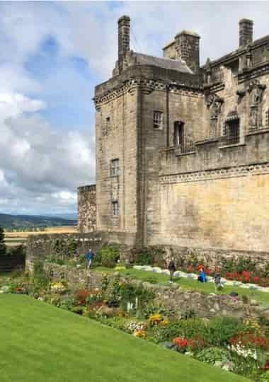 Stirling Castle in Scotland, with visitors walking through terraced gardens and countryside views in the background