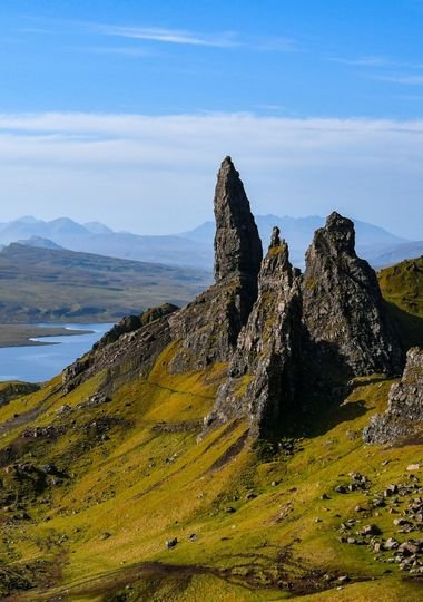 The Old Man of Storr rock pinnacle on the Isle of Skye, with a loch and misty mountains in the distance