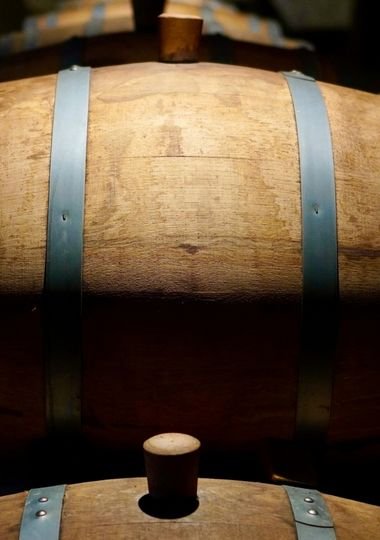 Close-up view of oak whisky casks with wooden bungs, stacked in a dimly lit warehouse