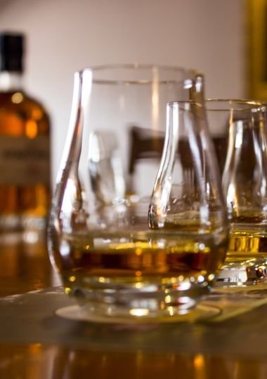 Glencairn glasses of whisky lined up on a bar with a whisky bottle in the background